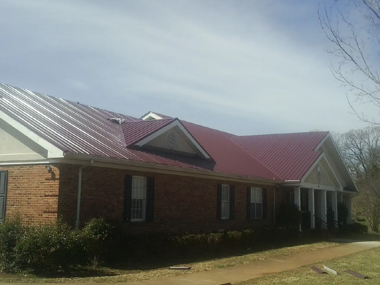 Red metal roof with gabled entries on a long brick building, from a Hail Damage Roof Repair job in Falmouth